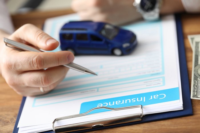 Hand mit Stift auf Versicheurngsunterlagen und kleinem Auto